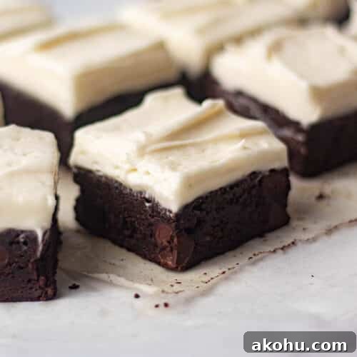 Angled view of sliced brownies with cream cheese frosting, highlighting the contrast between the rich chocolate base and the smooth, creamy topping. The dessert is perfect for chocolate lovers.