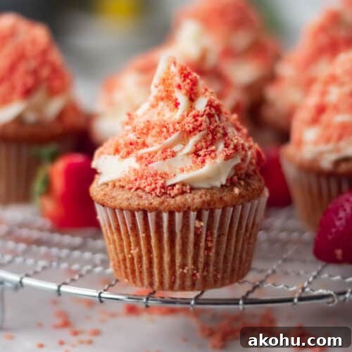 Gourmet strawberry crunch cupcakes with a delightful strawberry topping, set against a blurred kitchen background.
