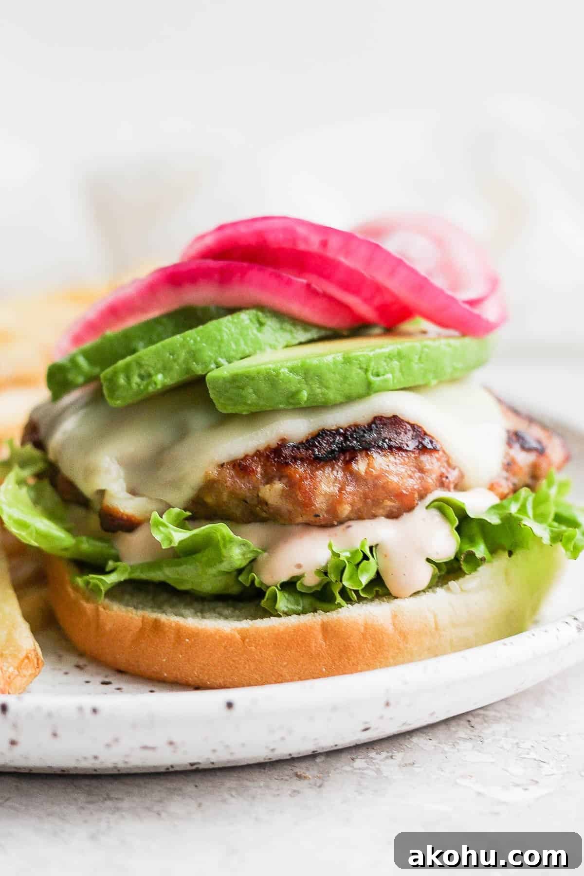 An avocado turkey burger on a bun with lettuce, burger sauce, avocado, and pickled onions.