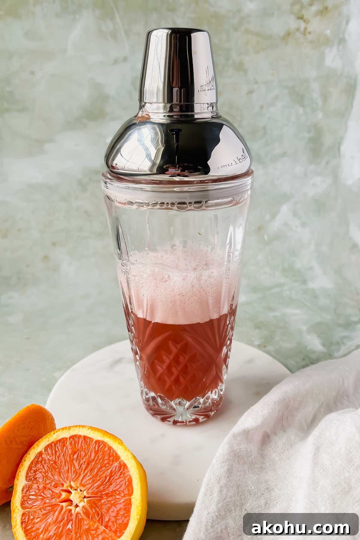 cranberry whiskey sour mixed in a glass cocktail shaker on green background.