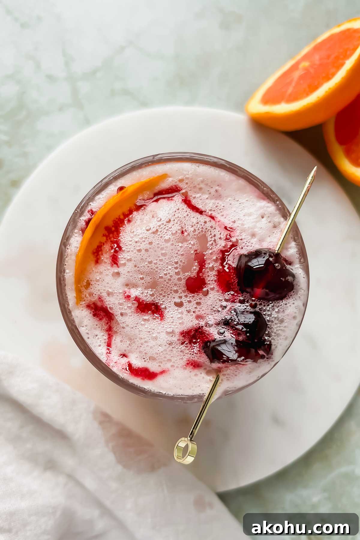 cranberry whiskey sour cocktail garnished with a spear of cocktail cherries and a orange peel.