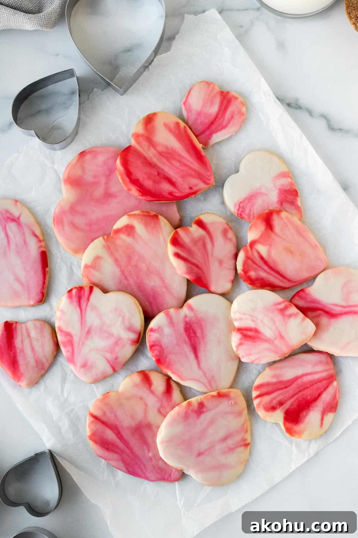 pile of red and pink marbled heart shaped sugar cookies on white parchment paper