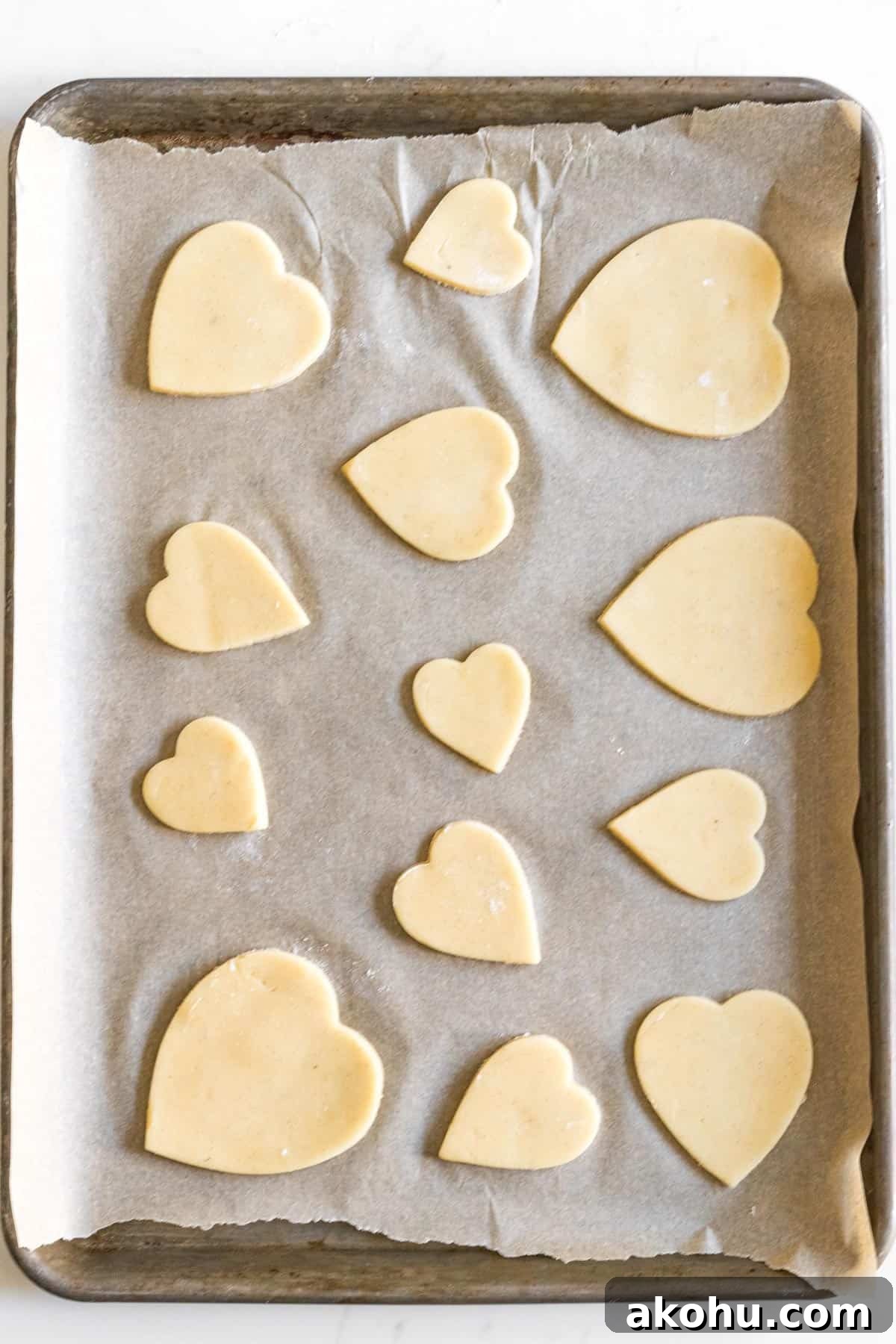sheet tray line with parchment paper with different sized heart cut out sugar cookies