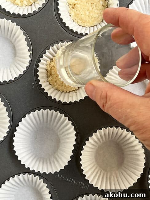 Hand holding a shot glass about to push down the crust in a white liner for the individual key lime pie bites.
