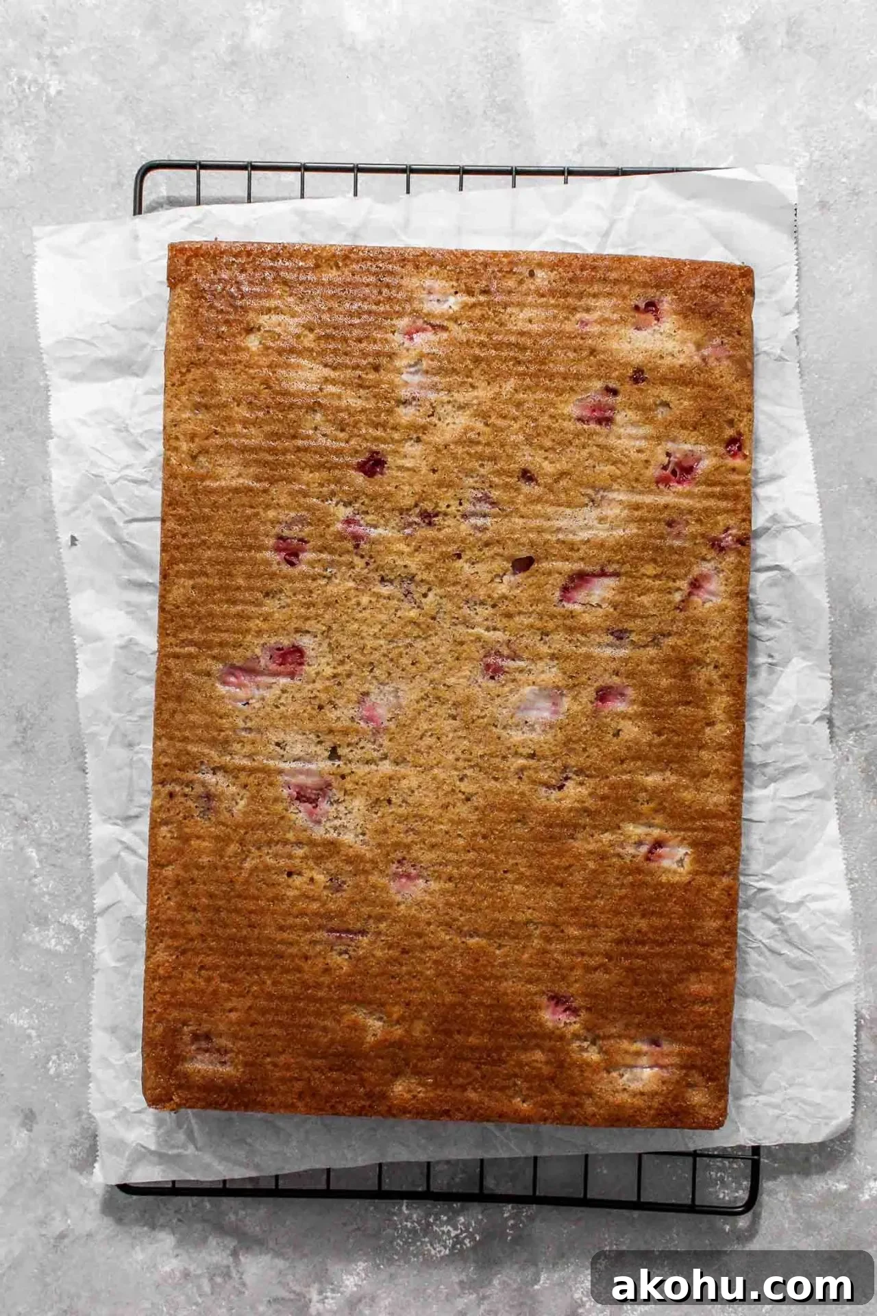 baked strawberry sheet cake on parchment lined wire rack