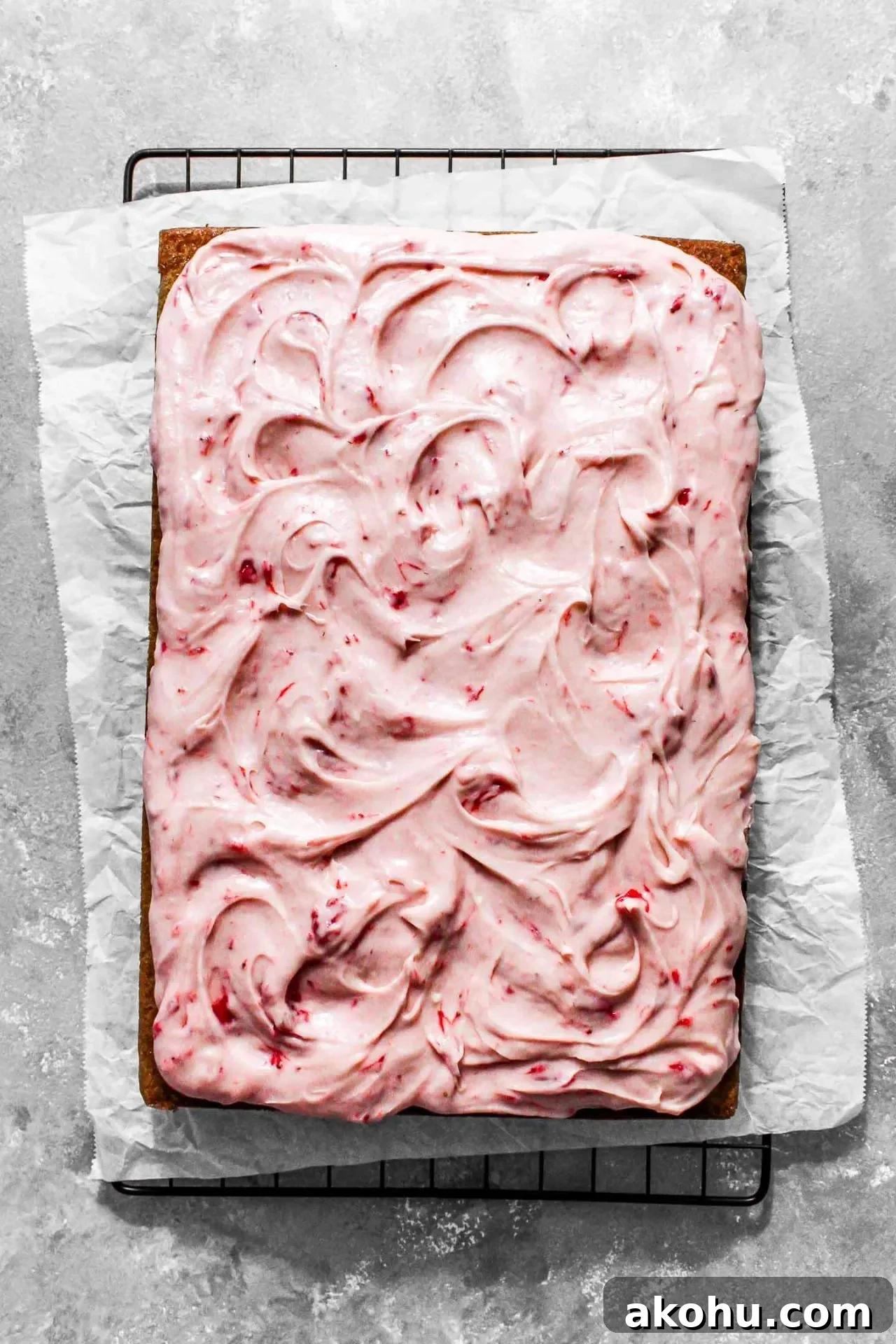 frosted strawberry sheet cake on parchment lined wire rack