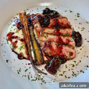Sous-Vide Duck Breast with Rainbow Carrots, Cauliflower & Cherry Gastrique 3 A gourmet plate featuring sliced duck breast with a rich berry sauce, accompanied by roasted carrots and a creamy white puree. Garnished with fresh herbs on a white plate.