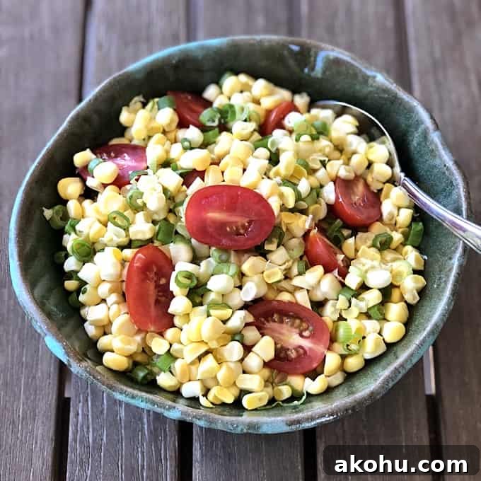 Summer Corn Tomato Salad in green ceramic bowl with spoon on wood table.