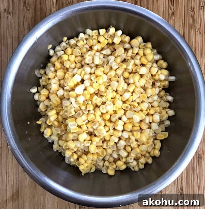 Fresh corn kernels in stainless bowl on wood table.