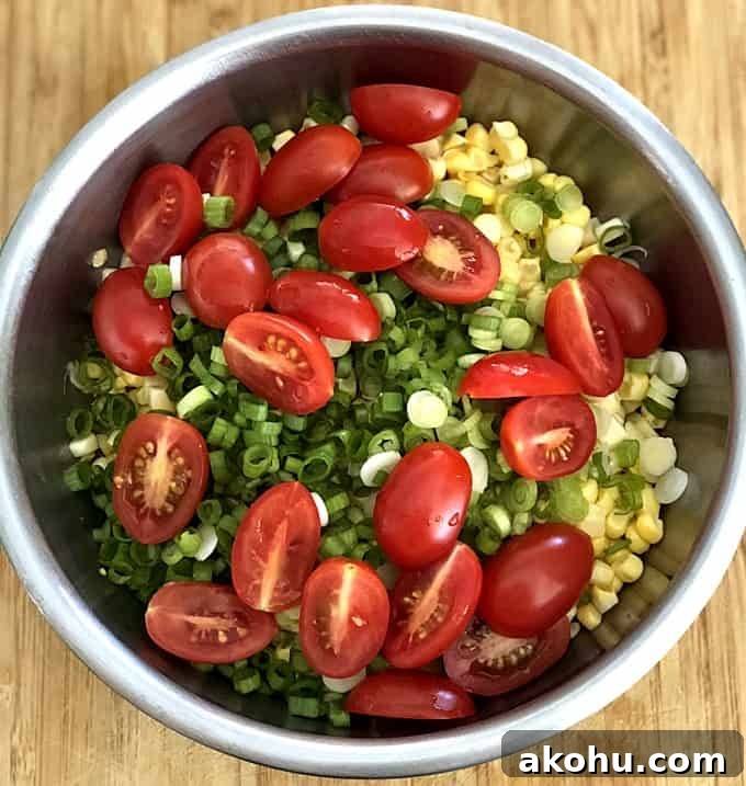 Cherry tomatoes, corn kernels and green onion in stainless bowl on wood table.