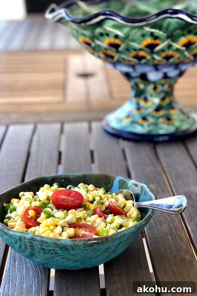 Corn and tomato salad in a green ceramic bowl on a wooden table with talavera pottery in the background.