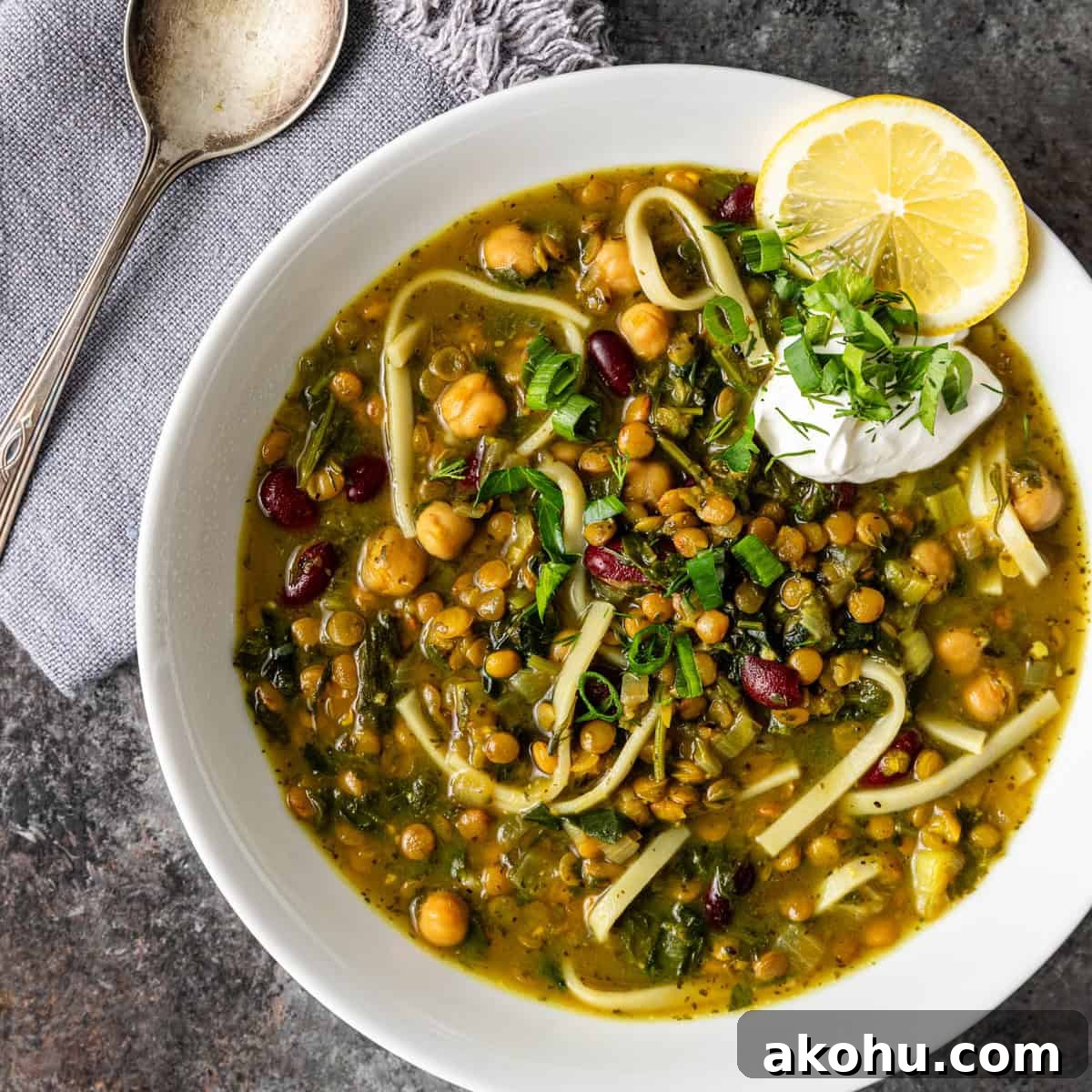 overhead: a big bowl of ash reshteh noodle soup with chickpeas, a lemon wedge and fresh cheese on top