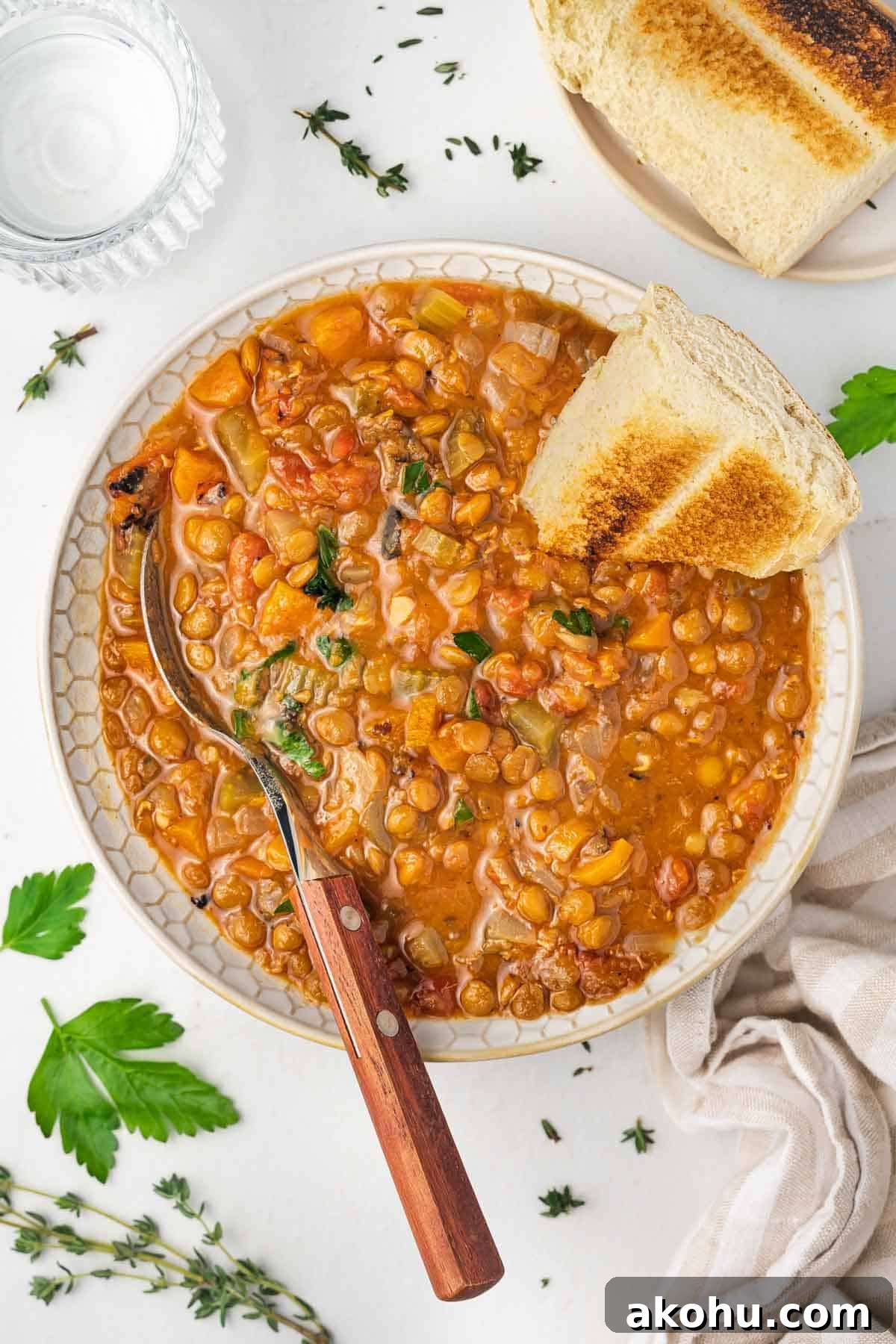 Overhead view of a bowl of slow cooker lentil soup with a piece of bread and spoon stuck into it.