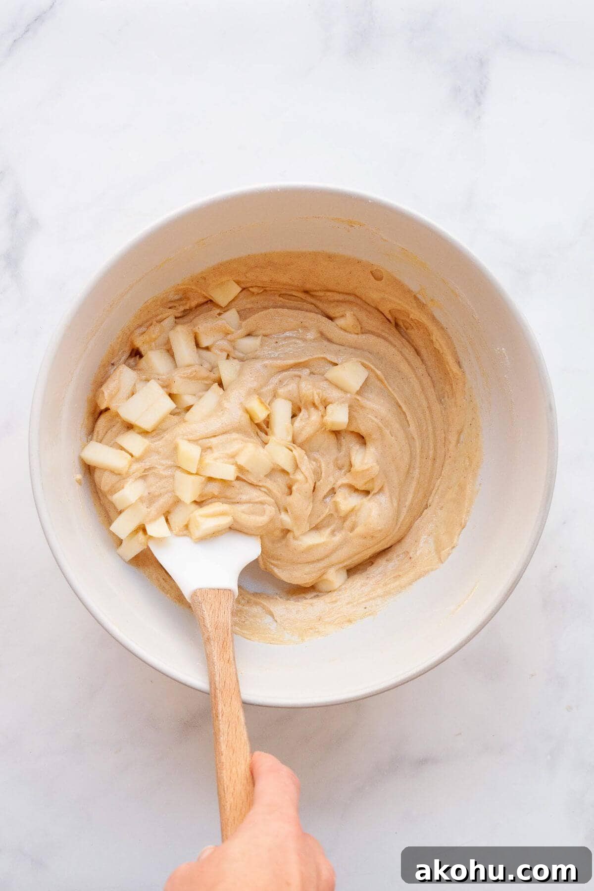 Gluten-Free Apple Cake: Moist Recipe with Cinnamon Crumble 6 Folding fresh apple chunks into gluten-free apple cake batter in a mixing bowl.