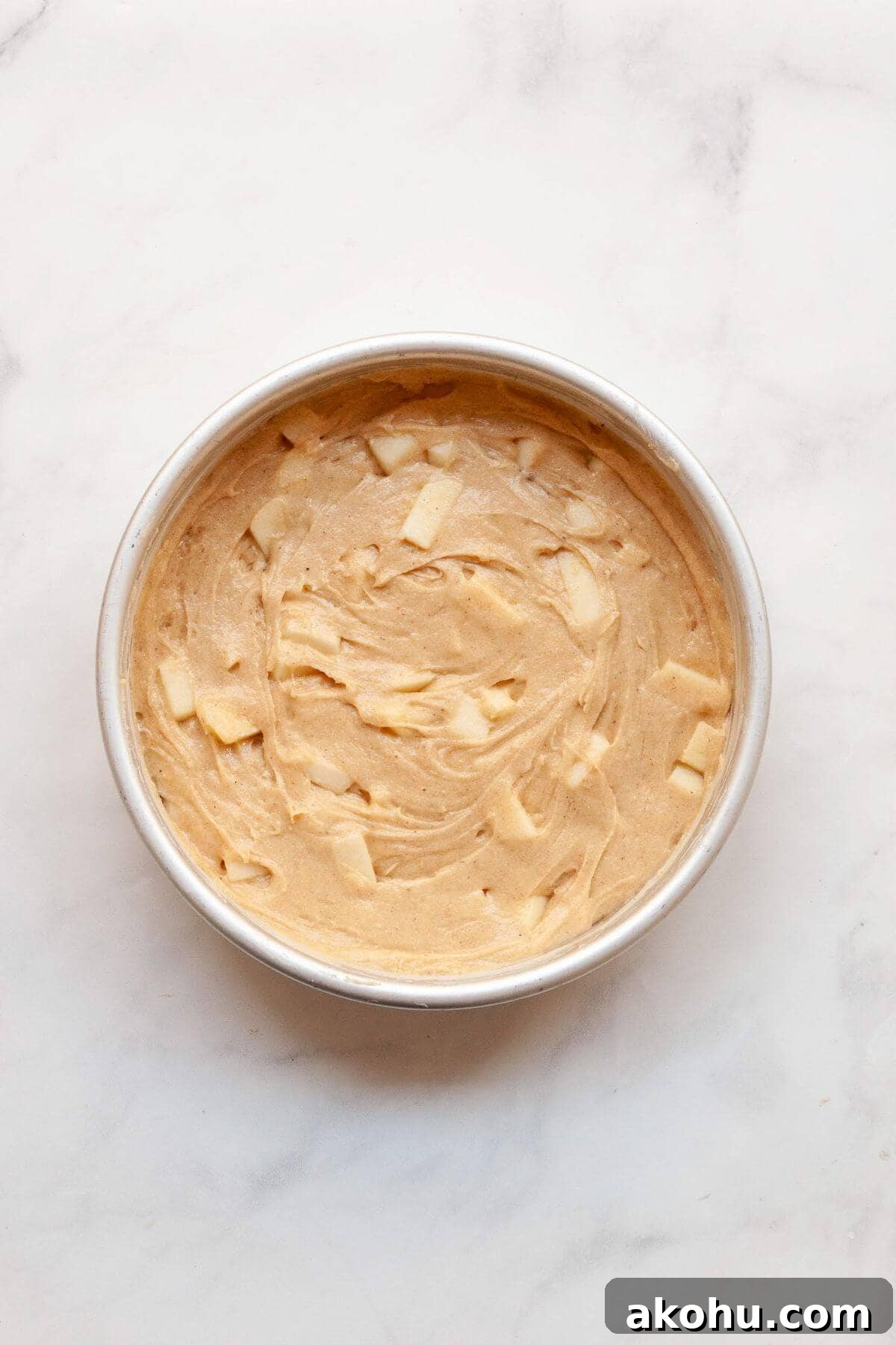 Gluten-Free Apple Cake: Moist Recipe with Cinnamon Crumble 7 Unbaked gluten-free apple cake batter with fresh apple chunks in a cake pan, ready to bake.