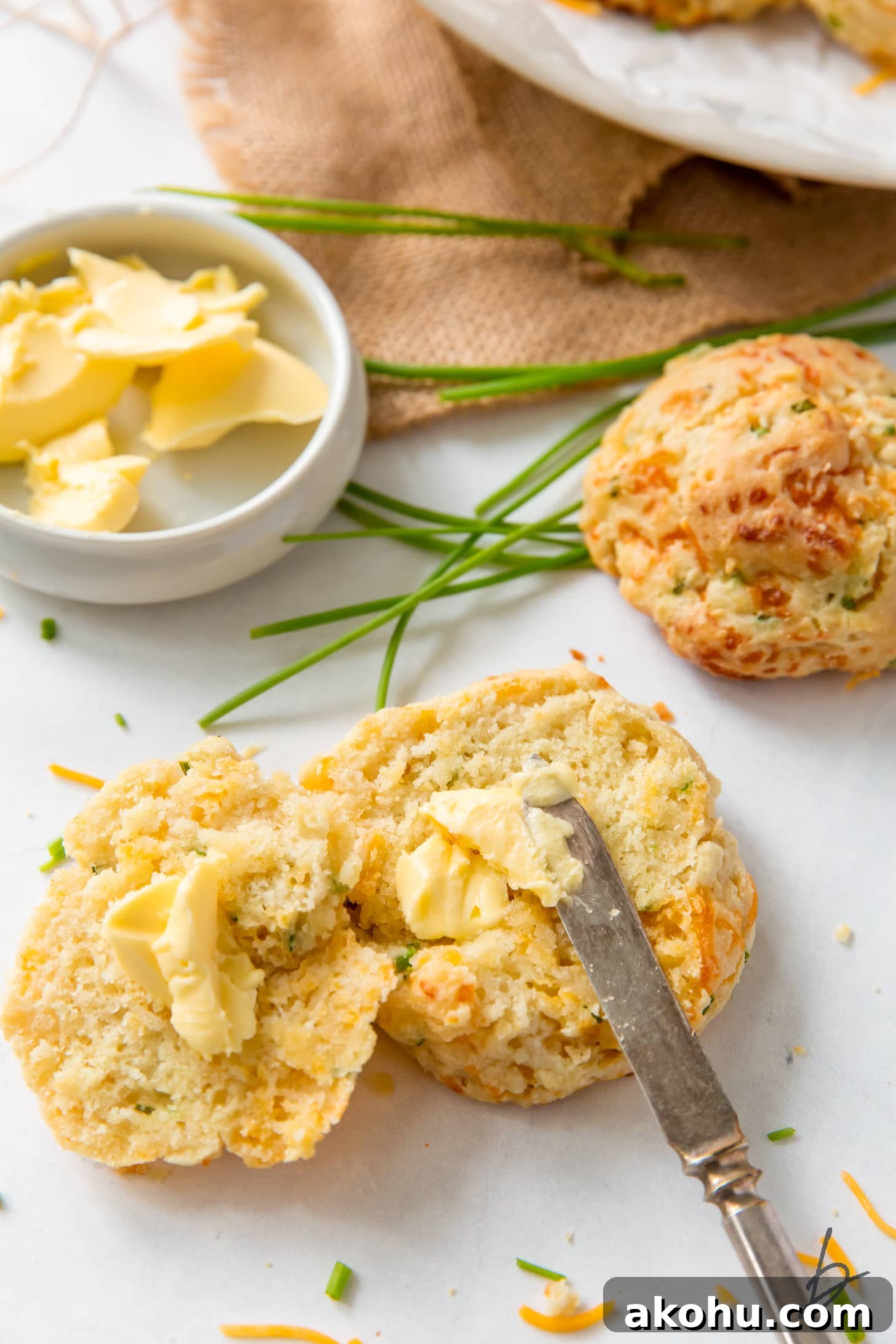 knife spreading butter in the center of a cheddar biscuit cut in half length wise
