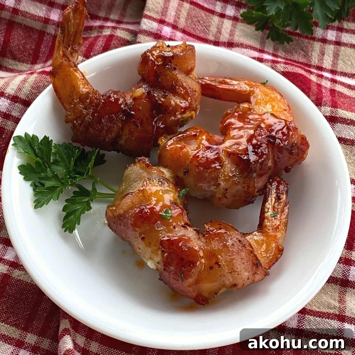 Three bacon wrapped shrimp stuffed with cream cheese and a jalapeno slice on a plate.