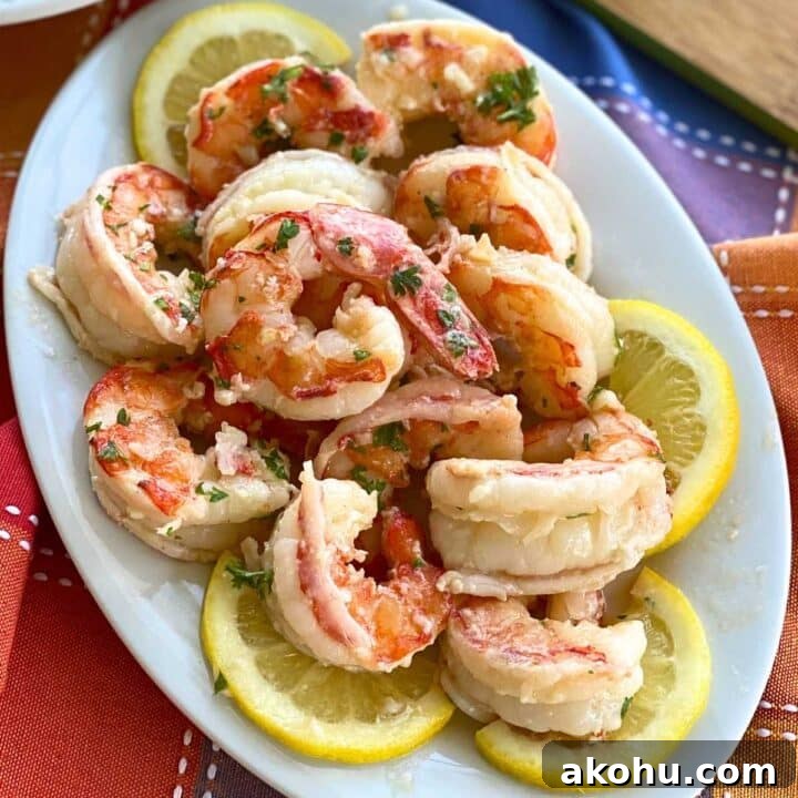 Argentine shrimp in a lemon, butter, garlic, scampi sauce on a white platter surrounded by slices of lemon.