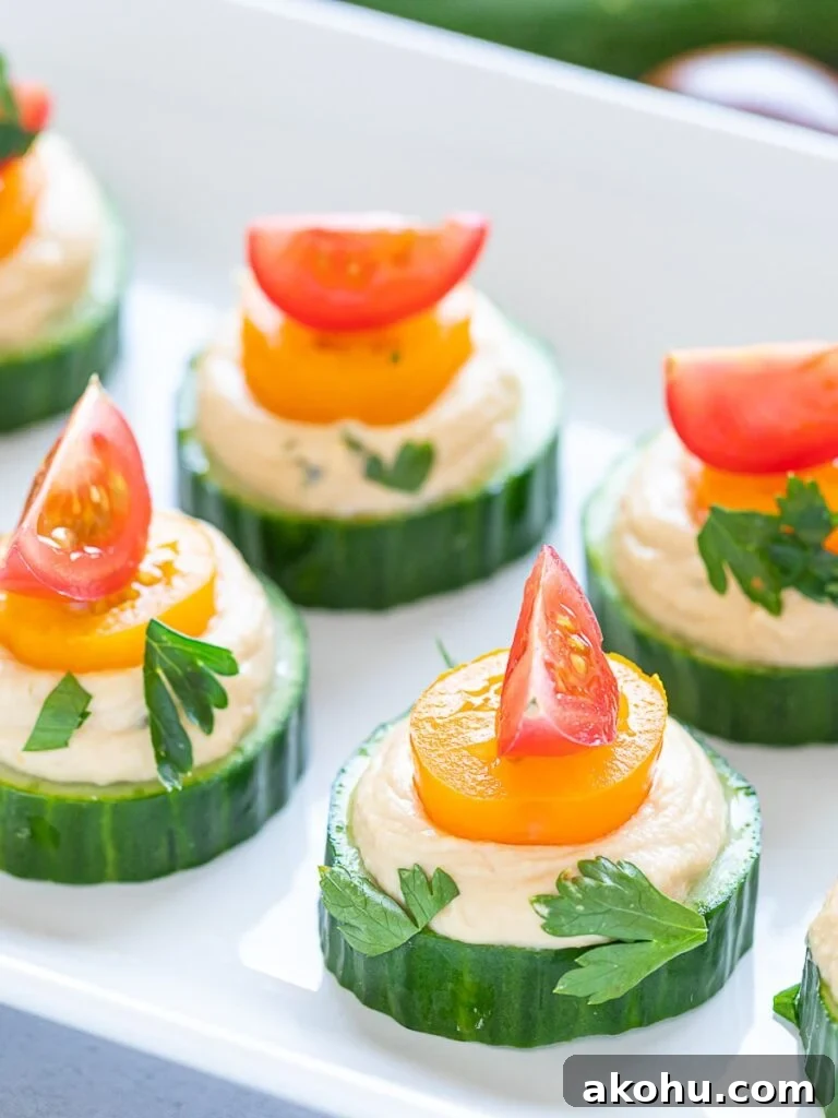 vegan cucumber hummus bites with red and orange cherry tomatoes on a white plate