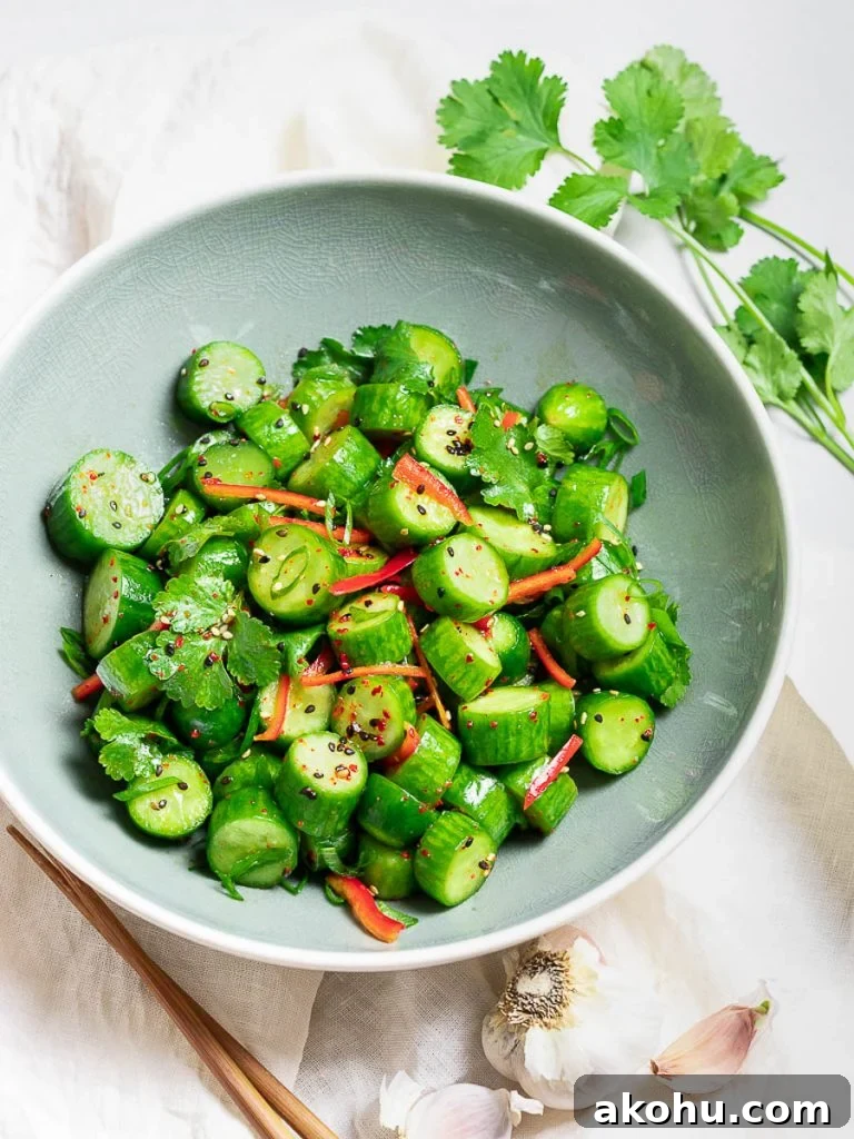 Spicy Asian cucumber salad with herbs and red pepper in a blue bowl next to garlic and chopsticks