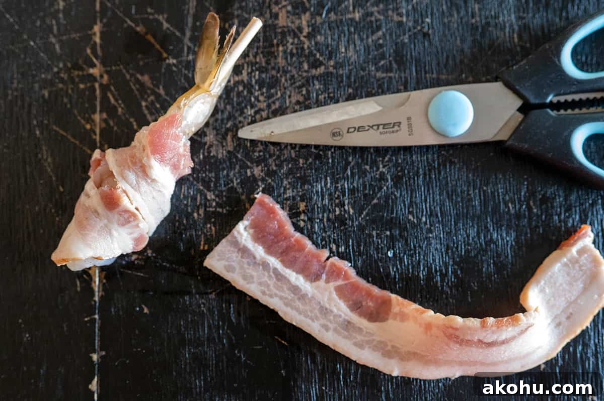 Half slice of bacon wrapped around shrimp with the other half on a board next to a pair of scissors.