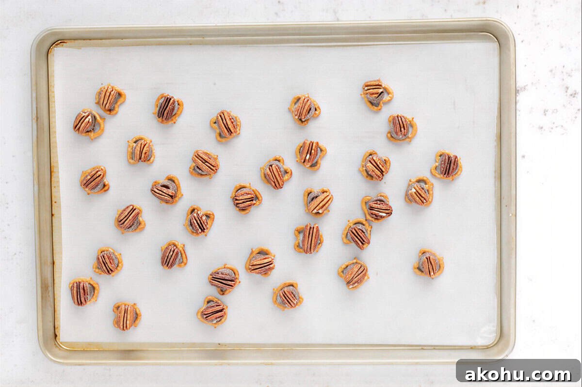 pecan-topped pretzel rolo turtles on a lined baking sheet.