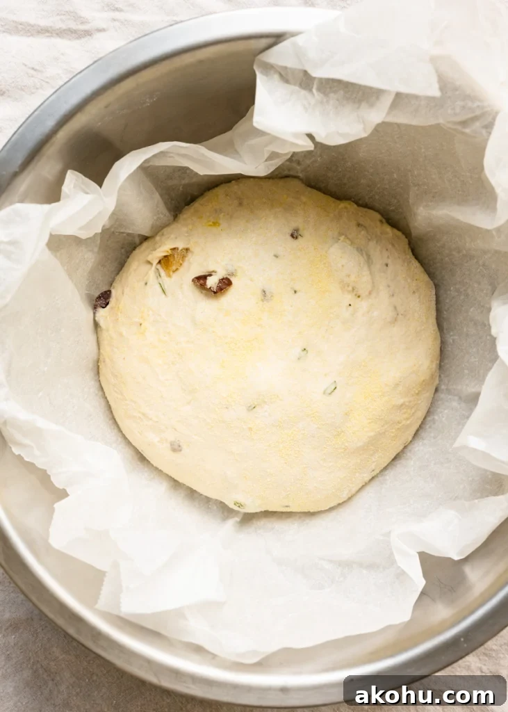 No-Knead Olive and Herb Artisan Bread Recipe 8 Overhead view of a bowl of bread dough inside a bowl lined with parchment paper.