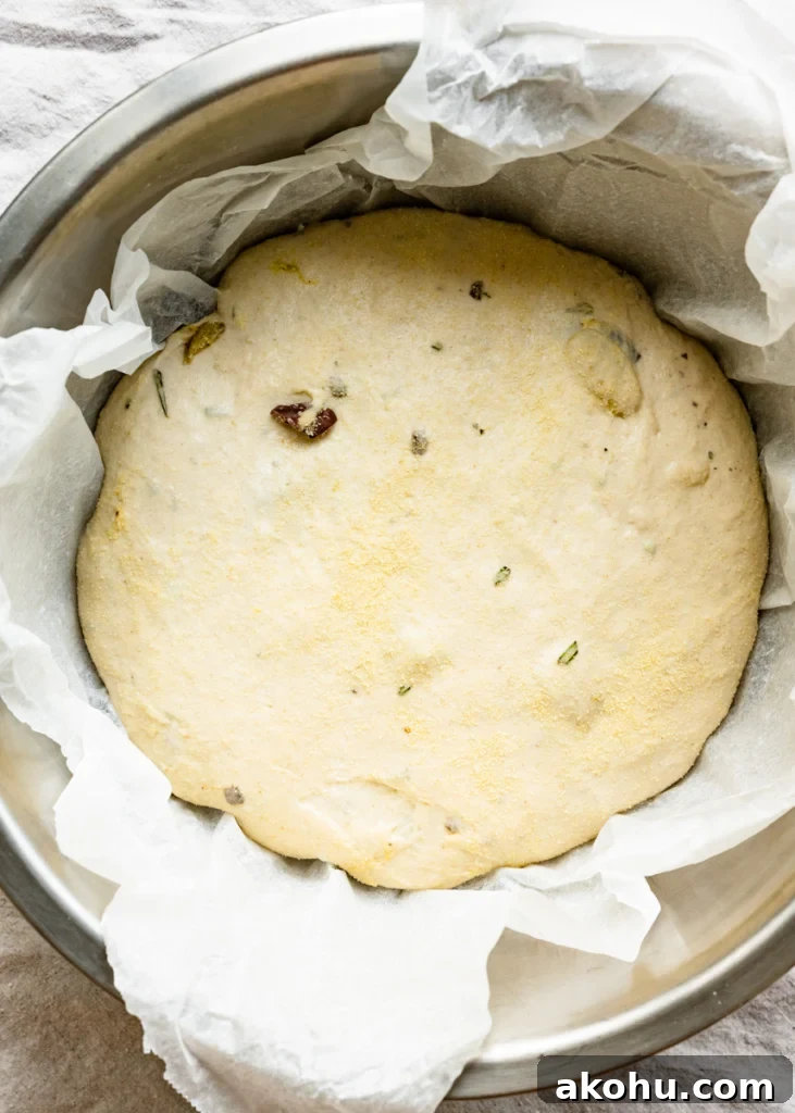 No-Knead Olive and Herb Artisan Bread Recipe 9 Overhead view of a bowl of bread dough inside a bowl lined with parchment paper.