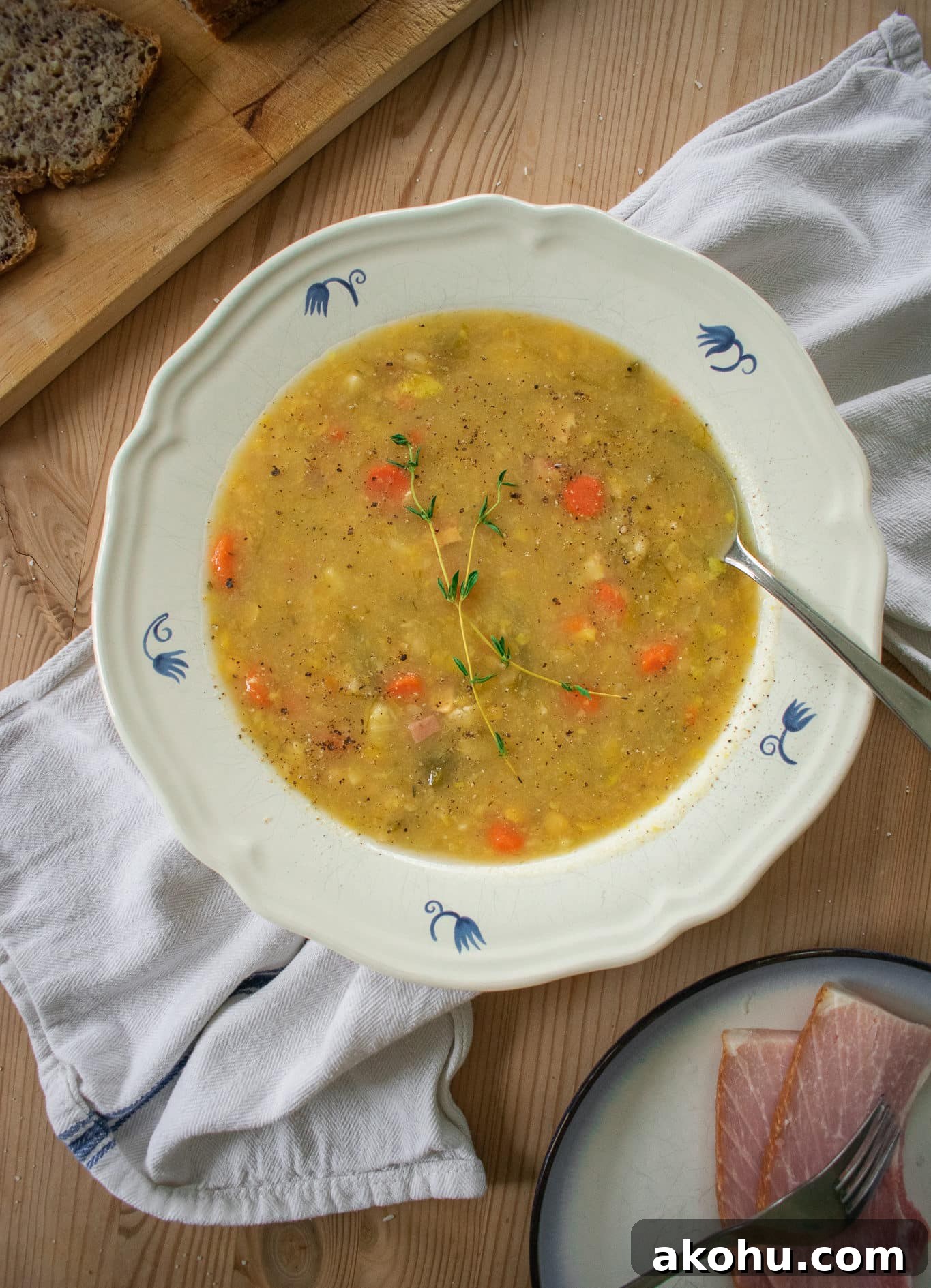 A bowl of split pea soup with rye bread and ham.