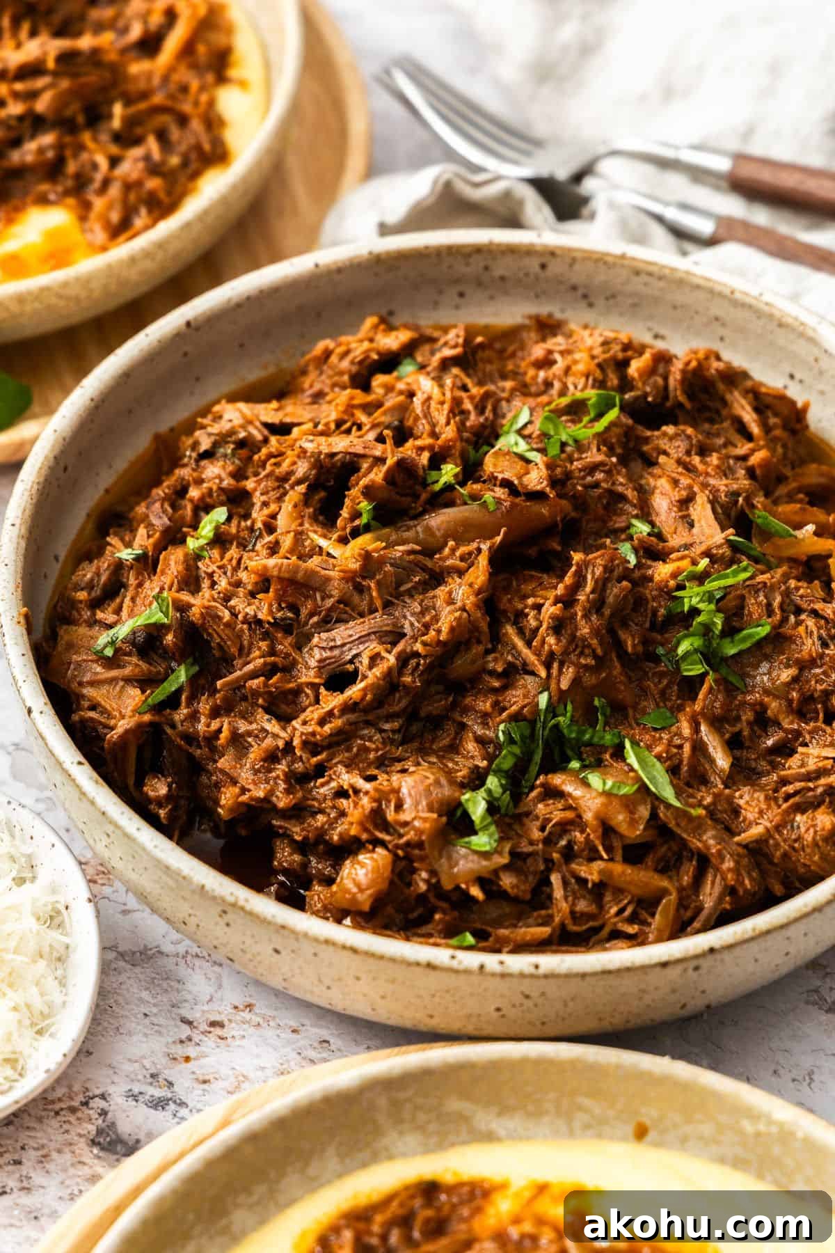 Easter Dinner Mains: Elegant Roast and Ham Recipes 11 Round dish of Mediterranean Pulled Beef garnished with fresh basil, sitting on a white cloth.