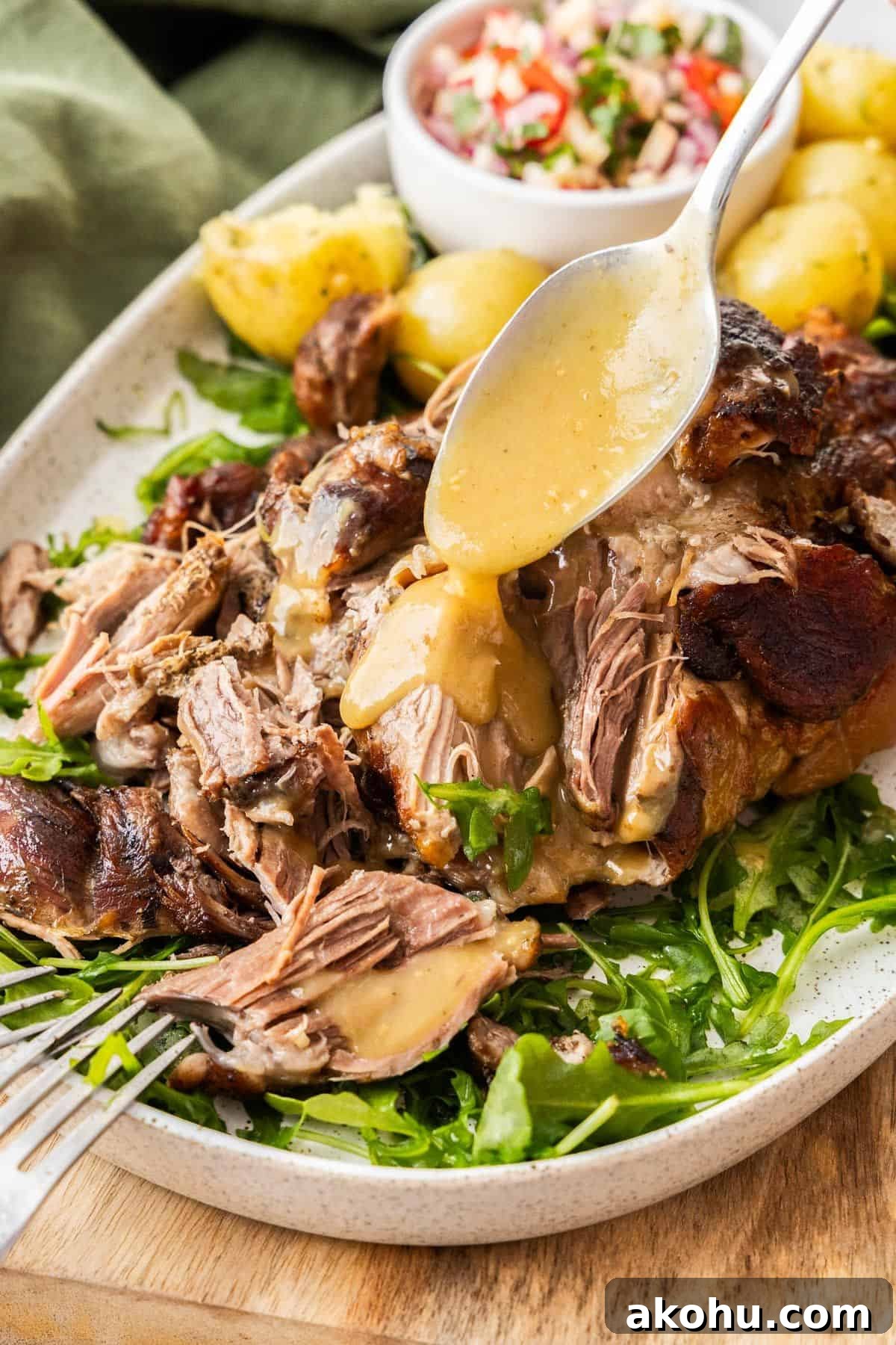 Easter Dinner Mains: Elegant Roast and Ham Recipes 14 Platter with Slow Roasted Pork Shoulder being drizzled with gravy, with some rocket leaves and potatoes around the edge.