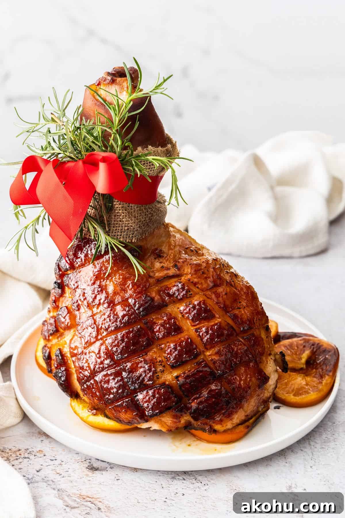 Easter Dinner Mains: Elegant Roast and Ham Recipes 15 Maple Glazed Ham, sitting on some orange slices on a round white plate.