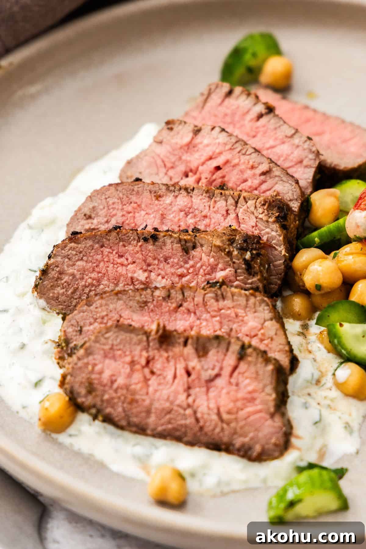 Easter Dinner Mains: Elegant Roast and Ham Recipes 21 Round grey plate with a serving of sliced Lamb Backstrap, sitting on yoghurt sauce, with a chickpea cucumber side salad.