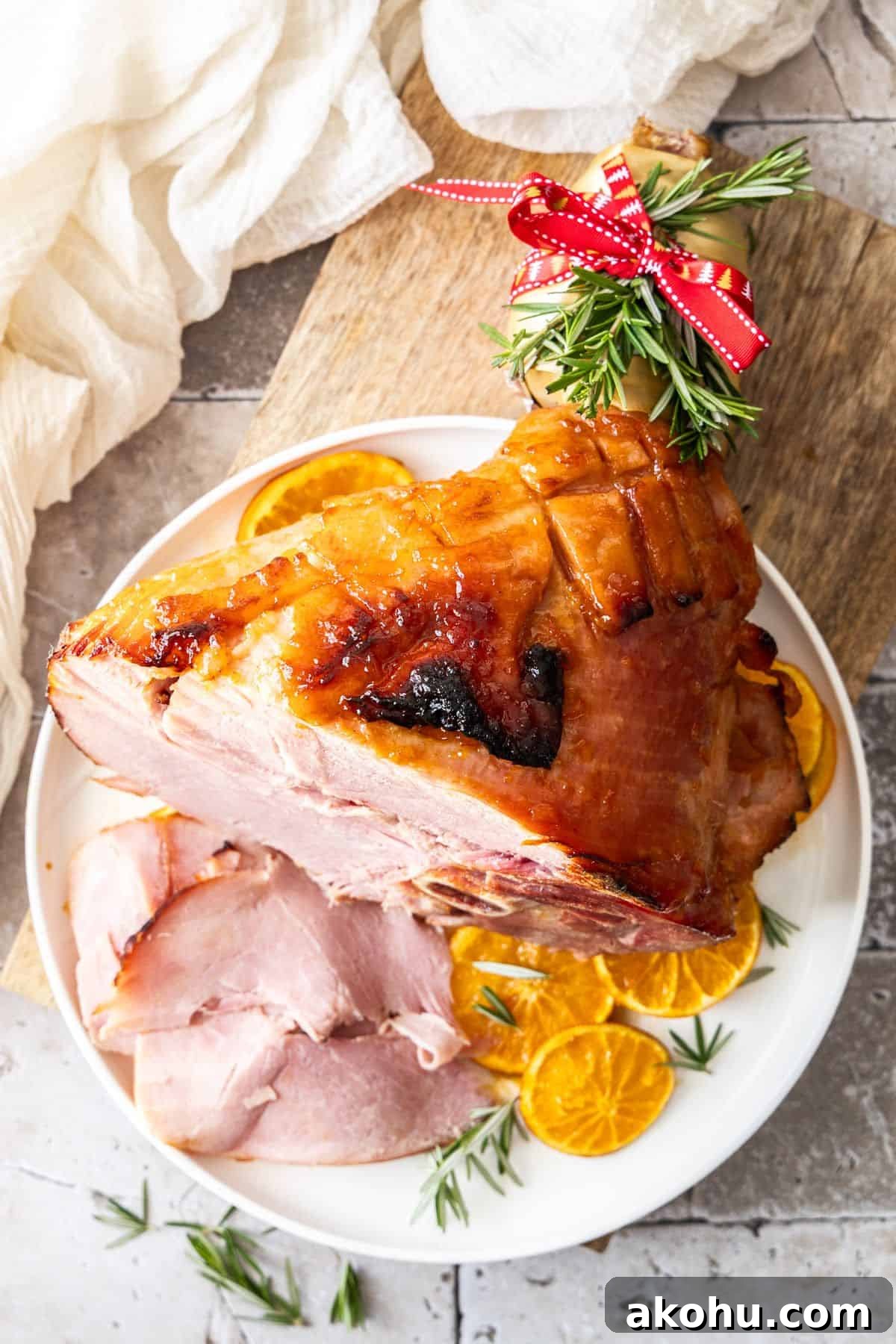 Easter Dinner Mains: Elegant Roast and Ham Recipes 4 Marmalade Glazed Ham, sitting on a round white plate, with some slices of ham cut, and orange slices around the edge.