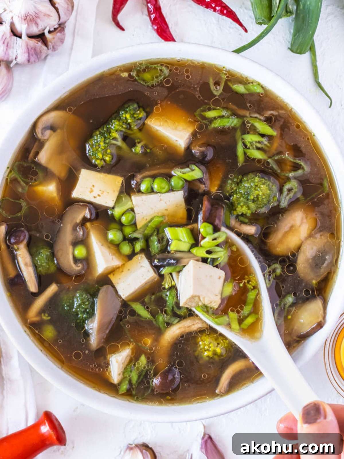 Top down view of tofu soup with noodles and broccoli in white bowl.