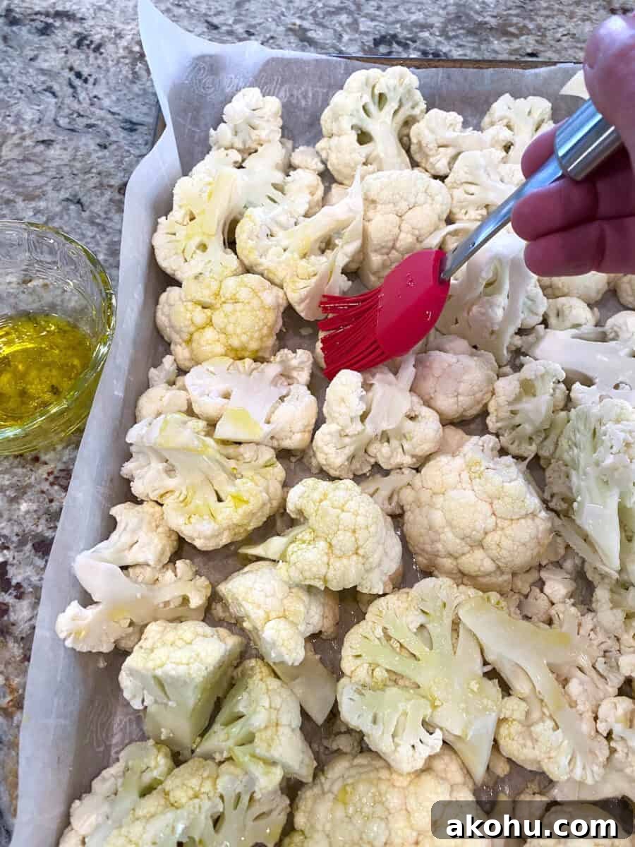 Raw cauliflower pieces on a baking pan being brushed with olive oil.