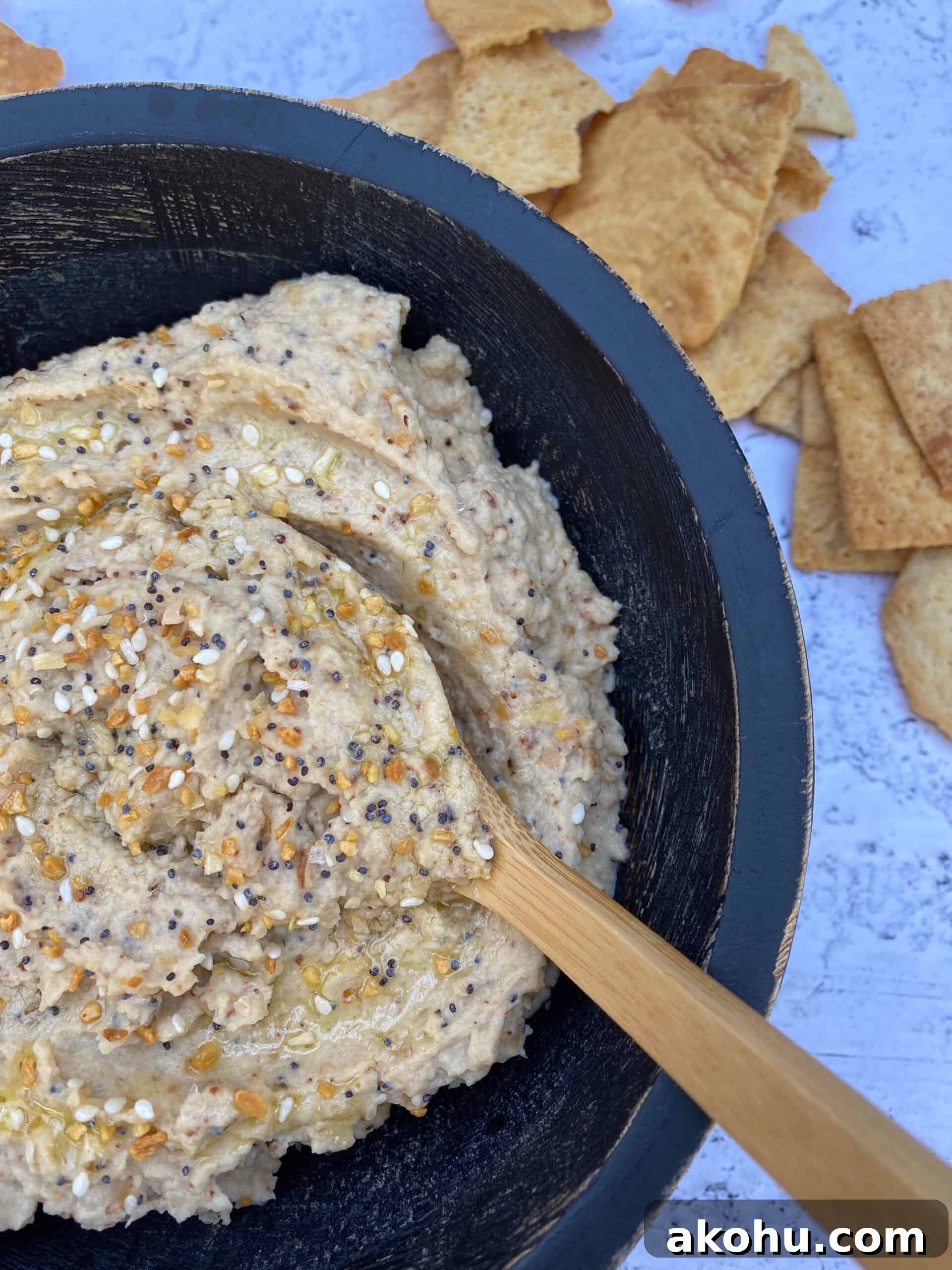 Hummus in a bowl with a small wooden spoon and pita chips on the side.