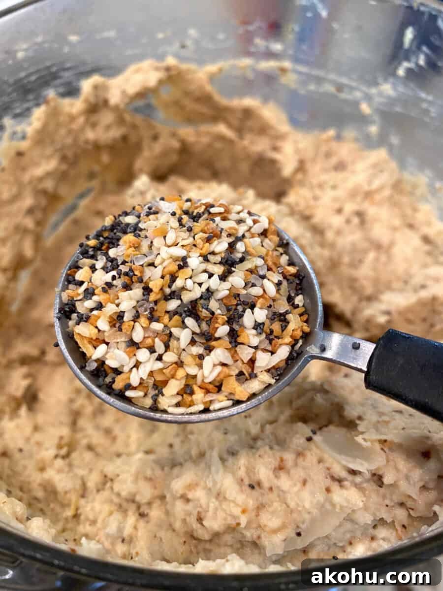 Everything Bagel seasoning on a tablespoon held over the blended cauliflower hummus.