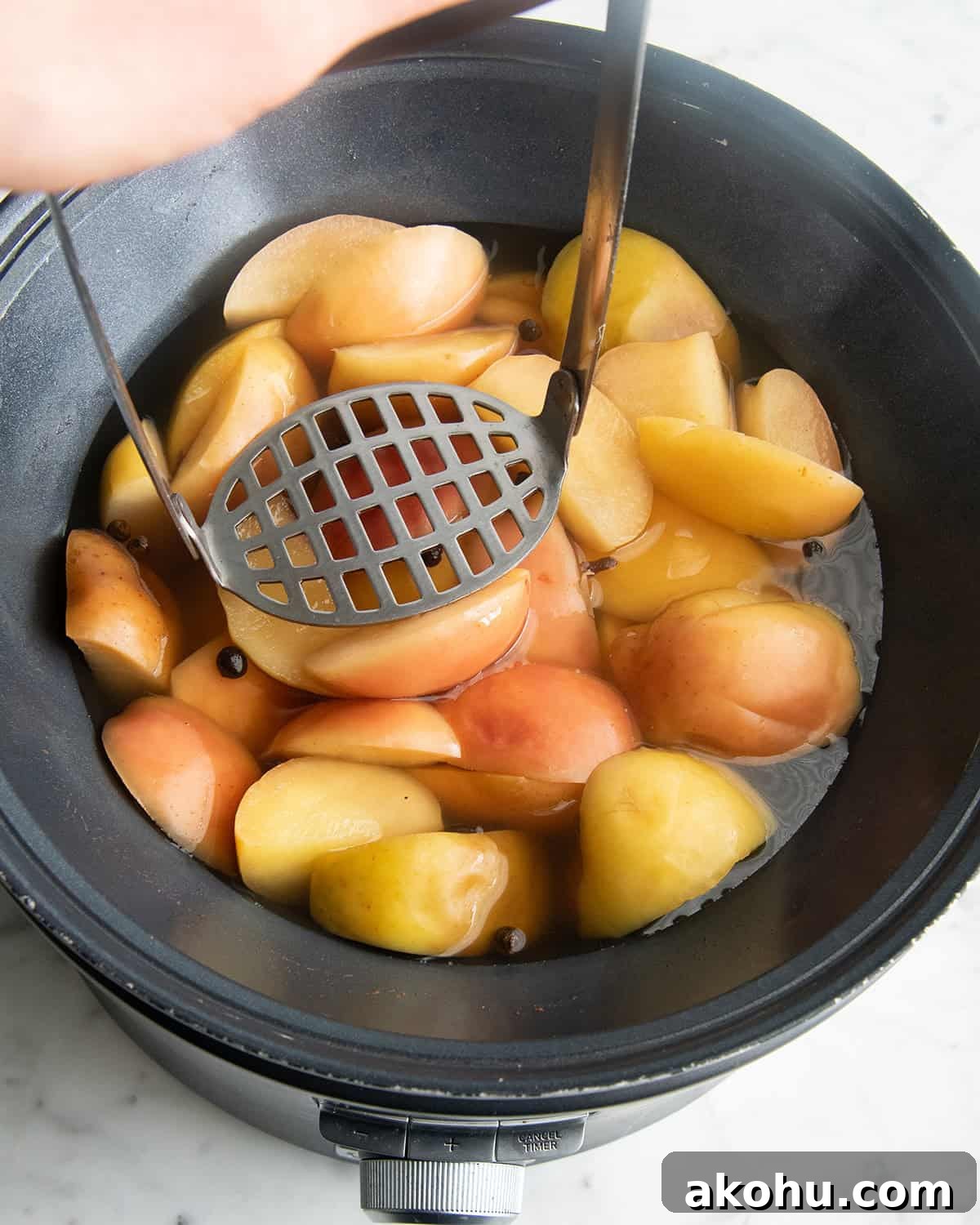 how to make apple cider recipe - a potato masher on top of the cooked cider ingredients in a crock pot