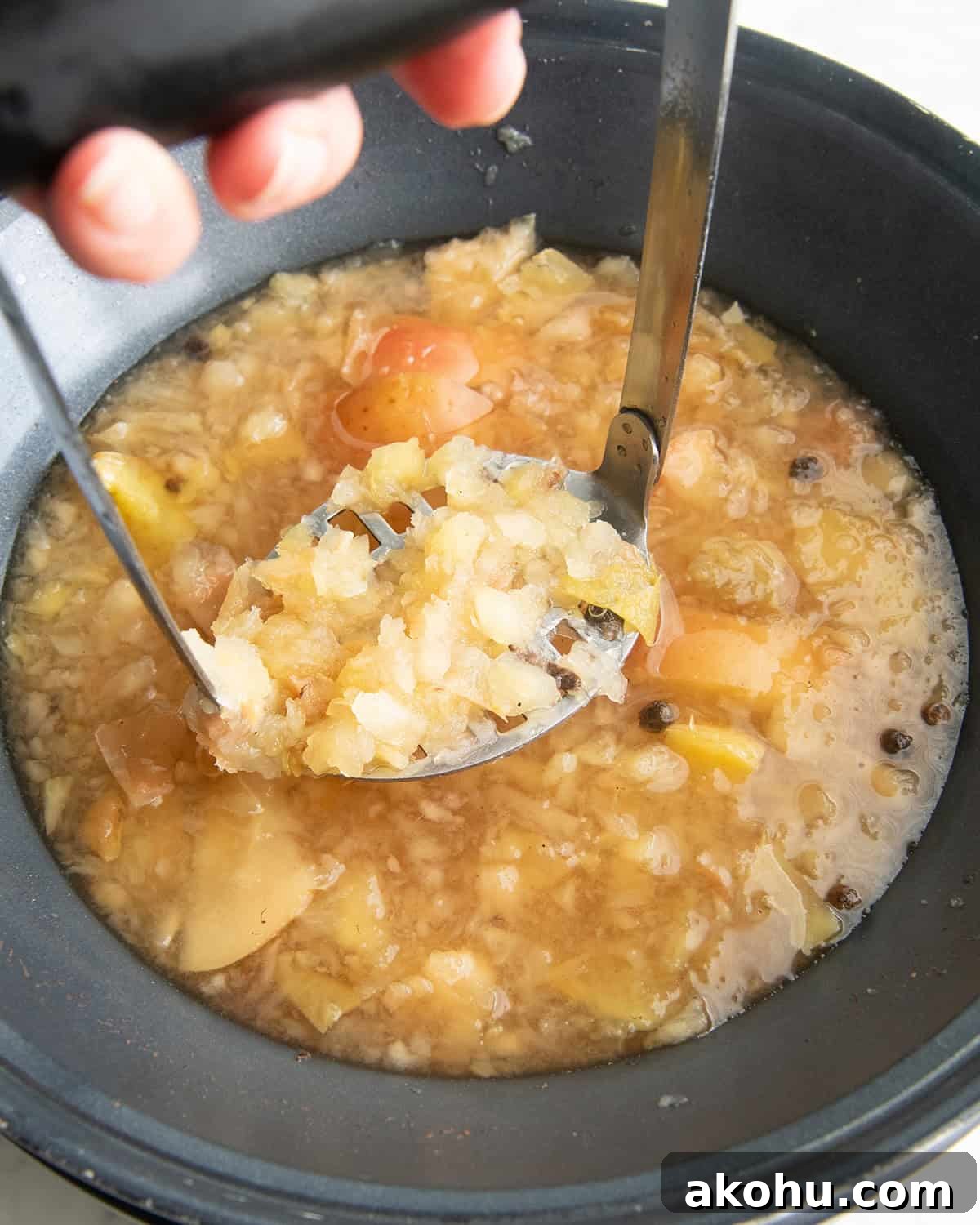 how to make apple cider recipe - a hand holding a potato masher mashing the apples