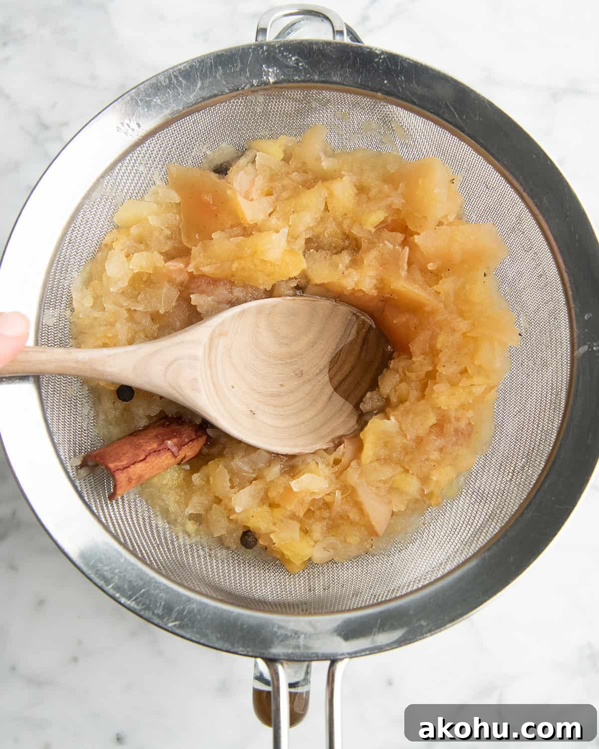 how to make apple cider recipe - overhead photo of a mixture being strained through a fine mesh metal strainer and pressed with a wooden spoon