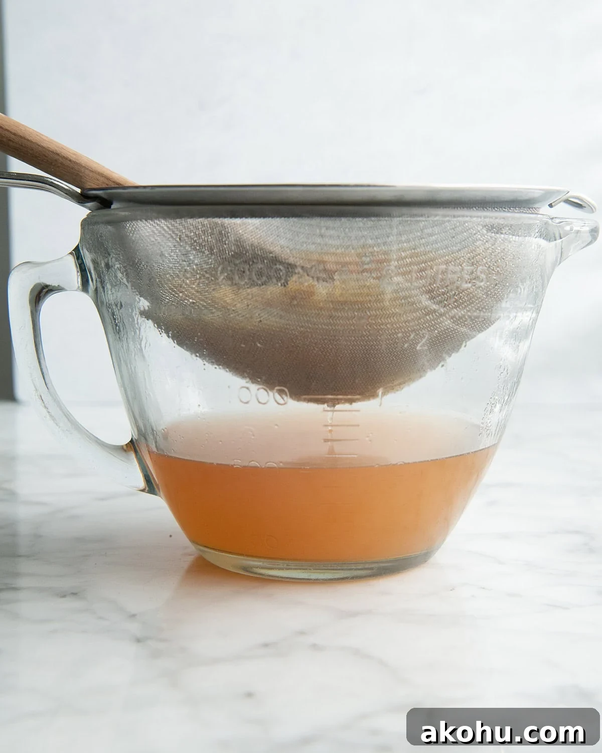 how to make apple cider recipe - front photo of a mixture being strained through a fine mesh metal strainer and pressed with a wooden spoon