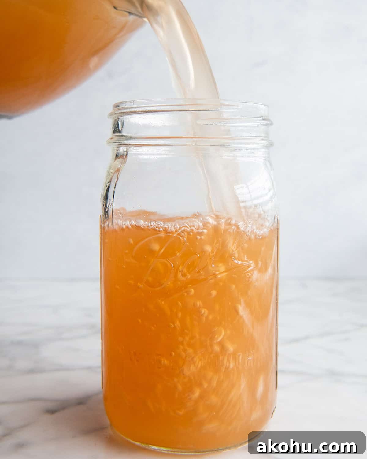 apple cider being poured from an 8 cup glass measuring cup into a large glass jar. 