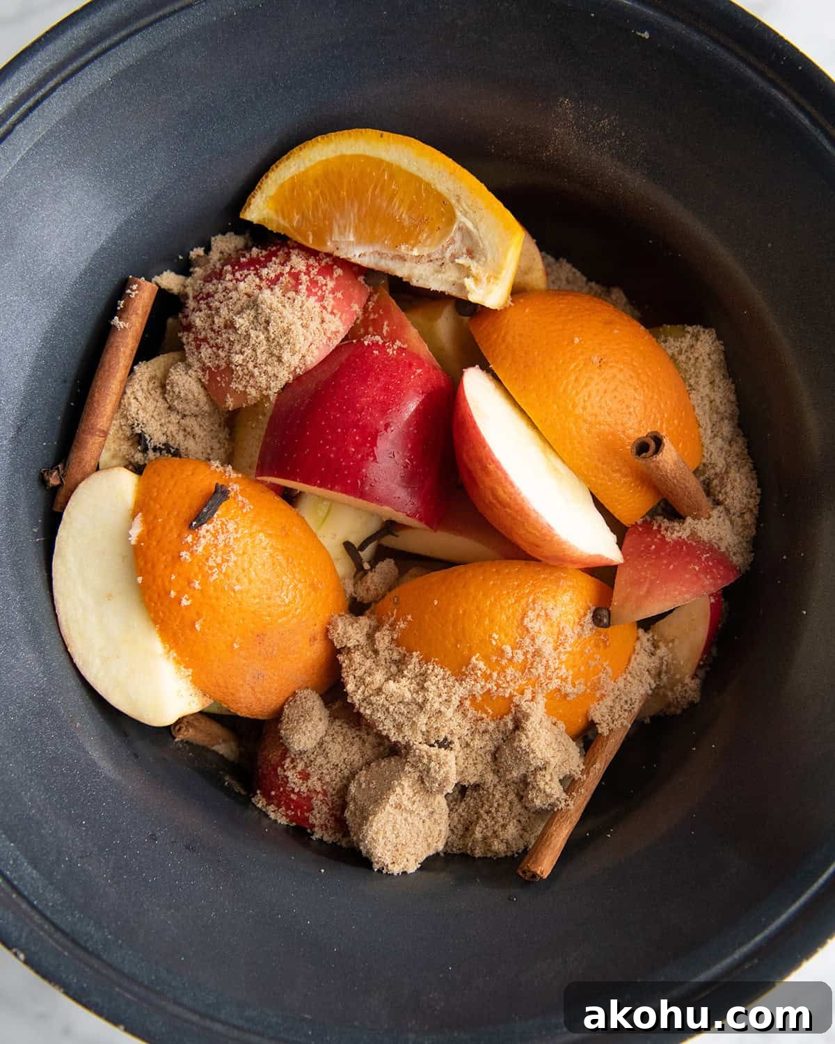 how to make apple cider recipe - ingredients apples, oranges, cinnamon sticks, brown sugar, cloves and nutmeg in a crock pot before cooking