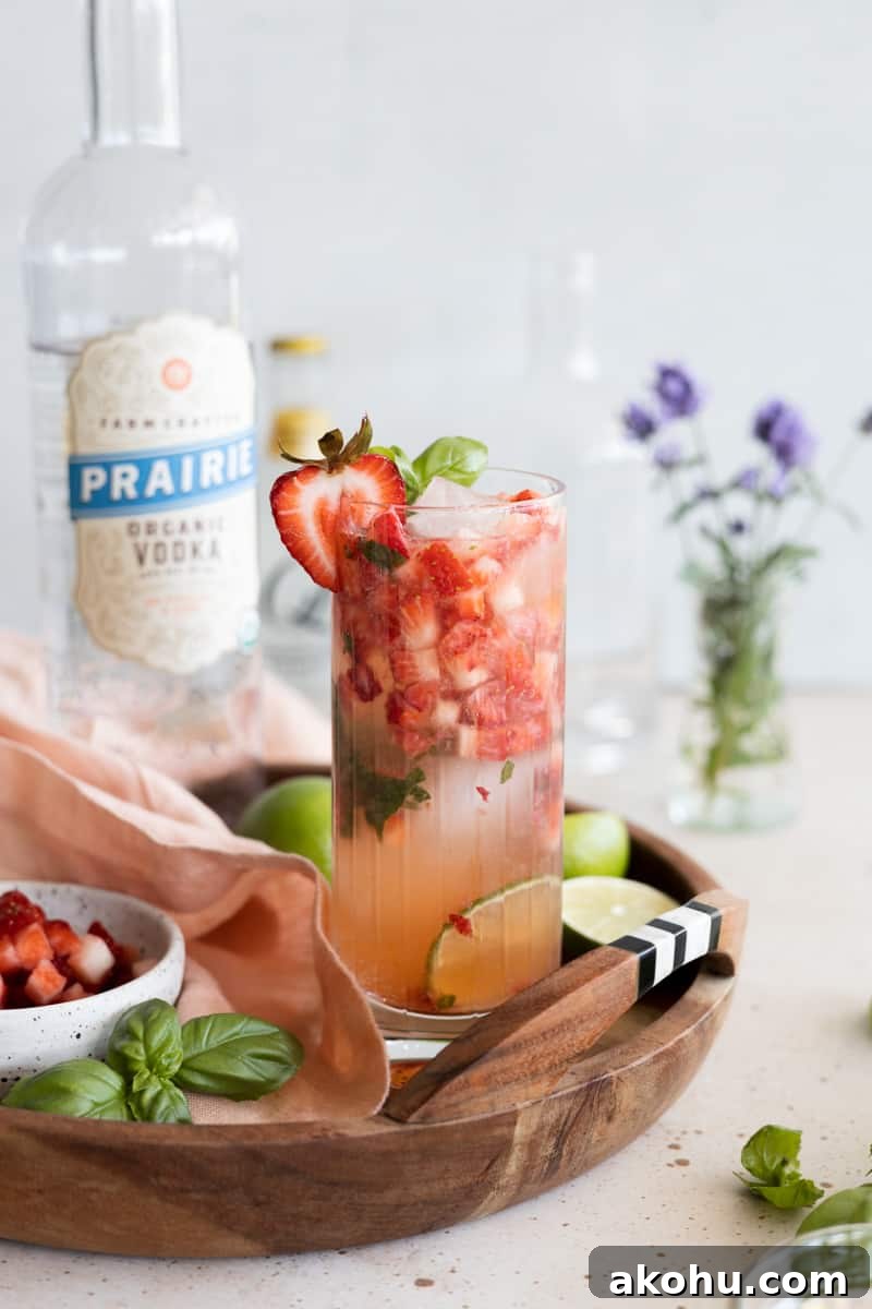 A strawberry basil vodka cocktail garnished with a strawberry slice on a wooden tray. 