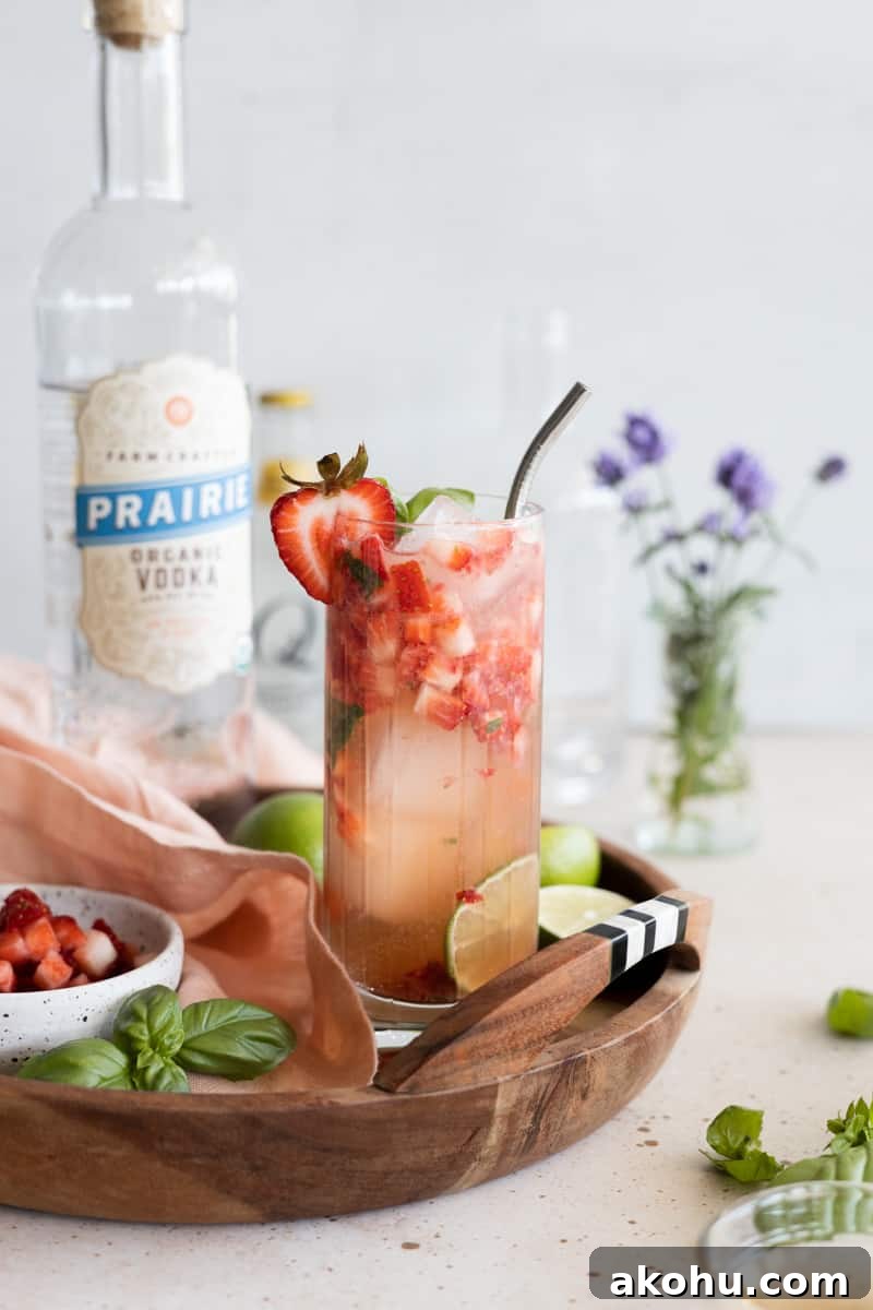 Strawberry basil vodka cocktail on a wooden tray with a straw. 