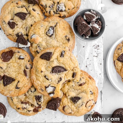 Oreo Stuffed Chocolate Chip Cookies: Gooey, Crunchy Dessert 11 cropped overhead shot of oreo chocolate chip cookies, with one cookie missing a bite on parchment lined cooling rack with oreos around.