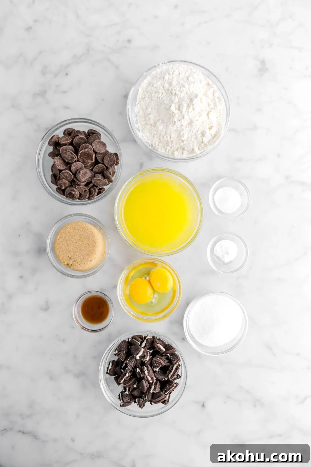 Oreo Stuffed Chocolate Chip Cookies: Gooey, Crunchy Dessert 5 flour, chocolate chips, melted butter, salt, baking soda, granulated sugar, chopped oreos, eggs, vanilla, and brown sugar on marble surface.