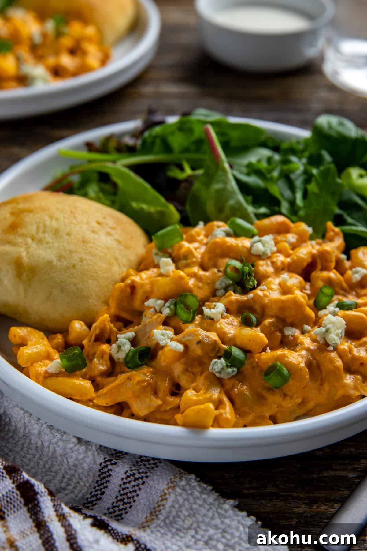 Cooked buffalo mac and cheese on a plate with a roll and simple salad.