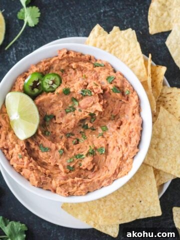 Bowl of vegan refried beans garnished with a lime wedge and surrounded by tortilla chips.